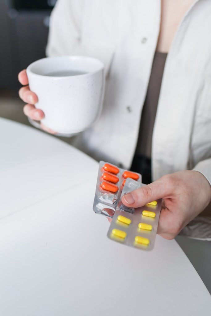 pexels photo 3873205 3873205 A woman holding blister packs of pills and a mug of tea, symbolizing treatment for illness.