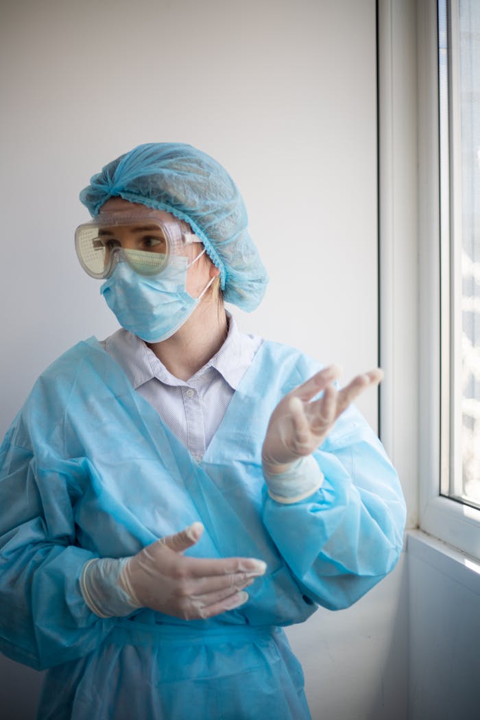 About A healthcare professional wearing PPE stands indoors looking out the window.