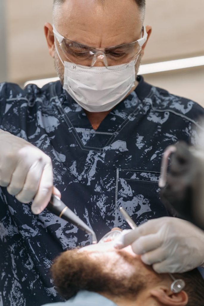 Dentist in protective gear conducting a dental procedure on a patient in a clinic setting.